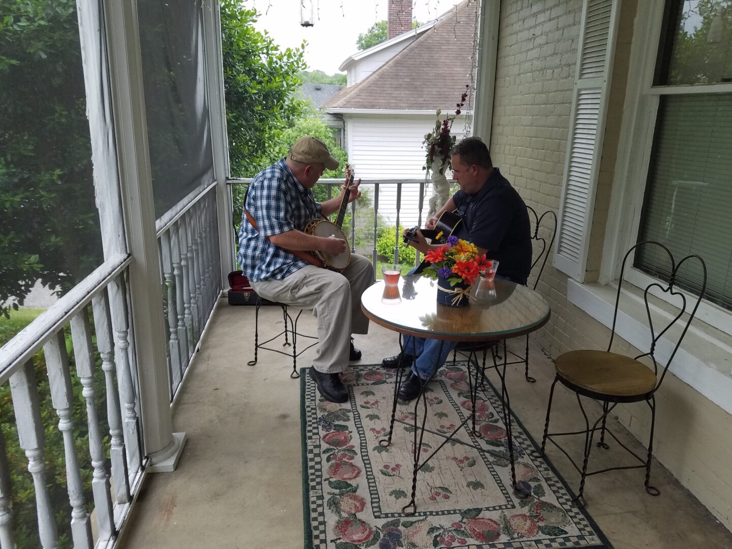 Two men sitting on a porch with a table and chairs.